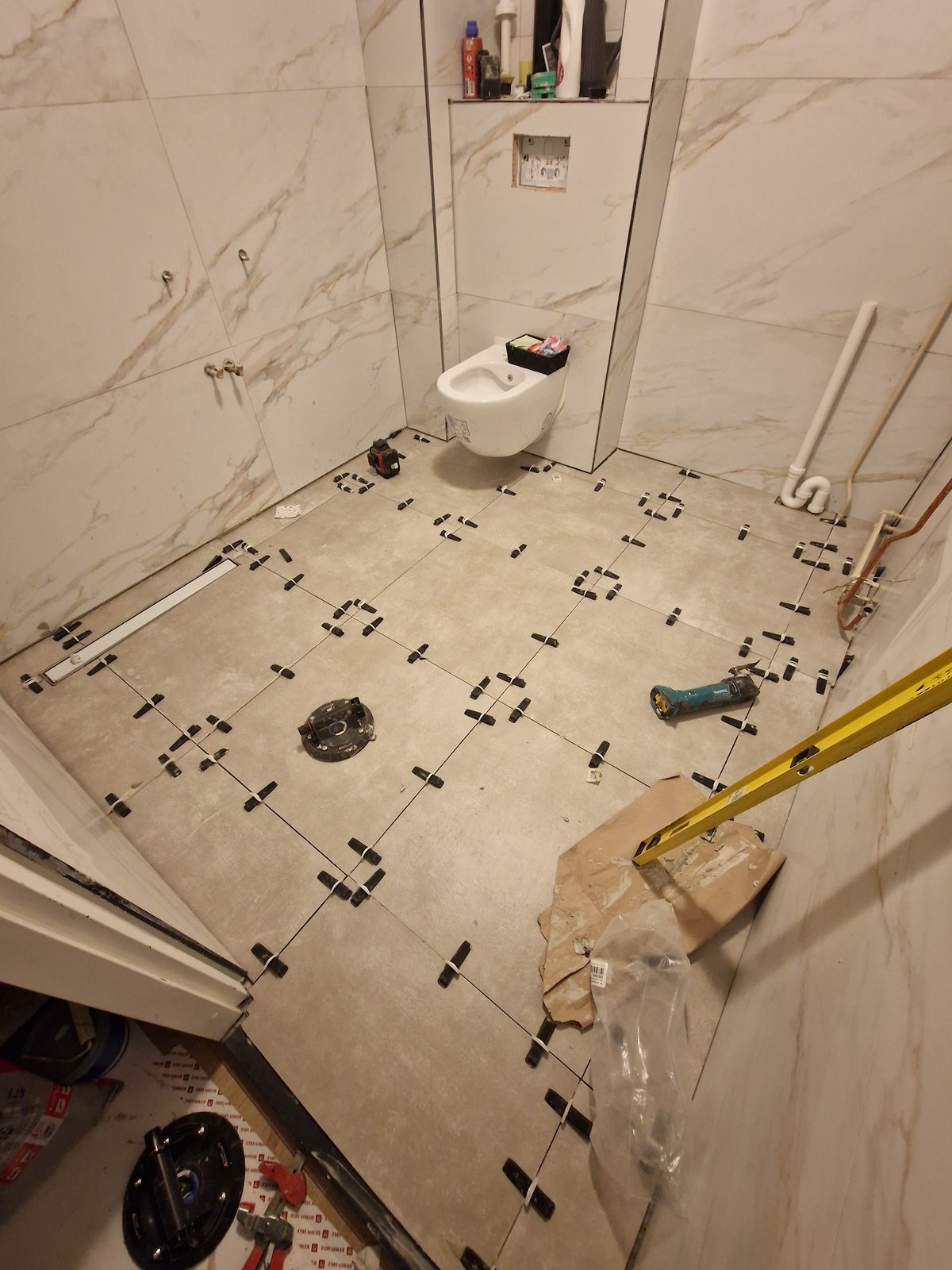 Een badkamer in aanbouw met grote tegels in marmerlook en een hangend toilet