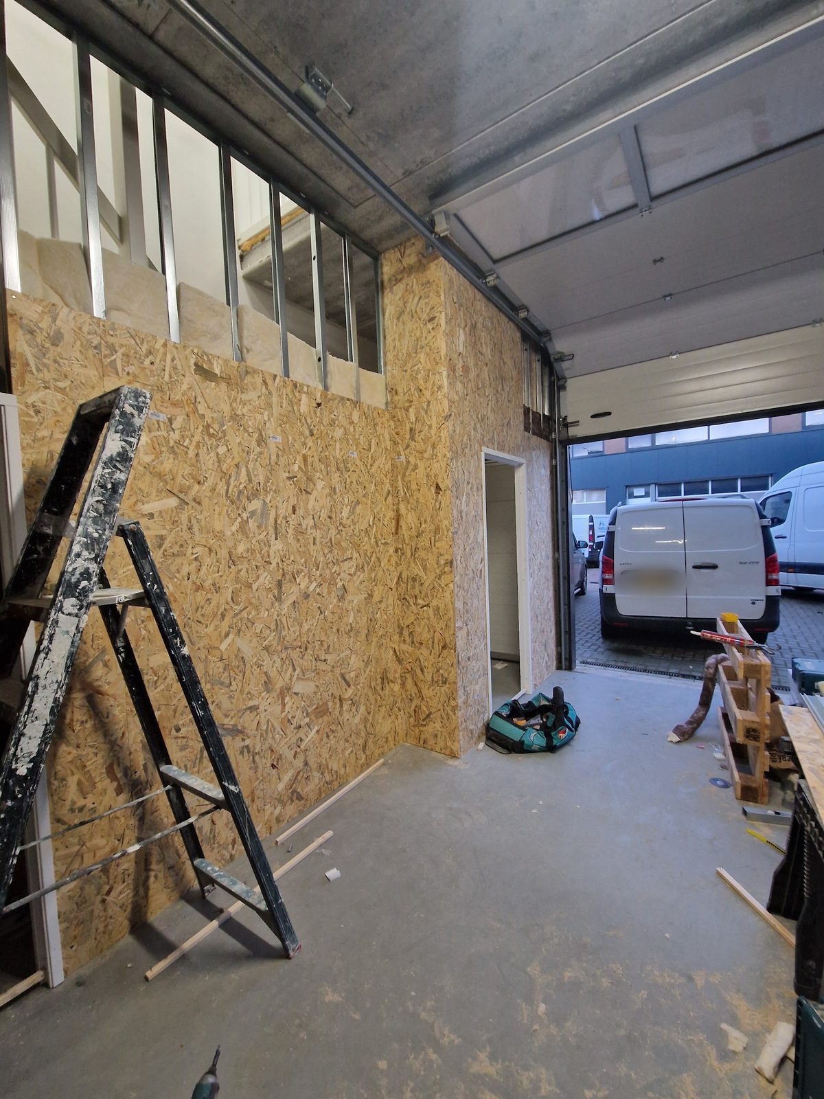 Een bedrijfsruimte met nieuwe wanden van OSB en metal stud, de roldeur open naar het bedrijventerrein