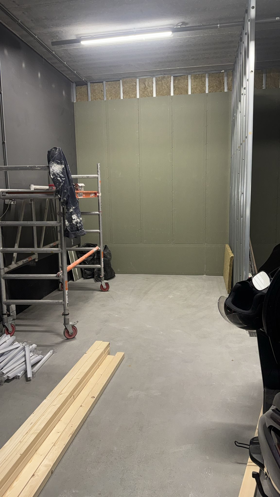 Een ruimte met een nieuwe wand van metal stud en groene platen, een rolsteiger en balken op de vloer